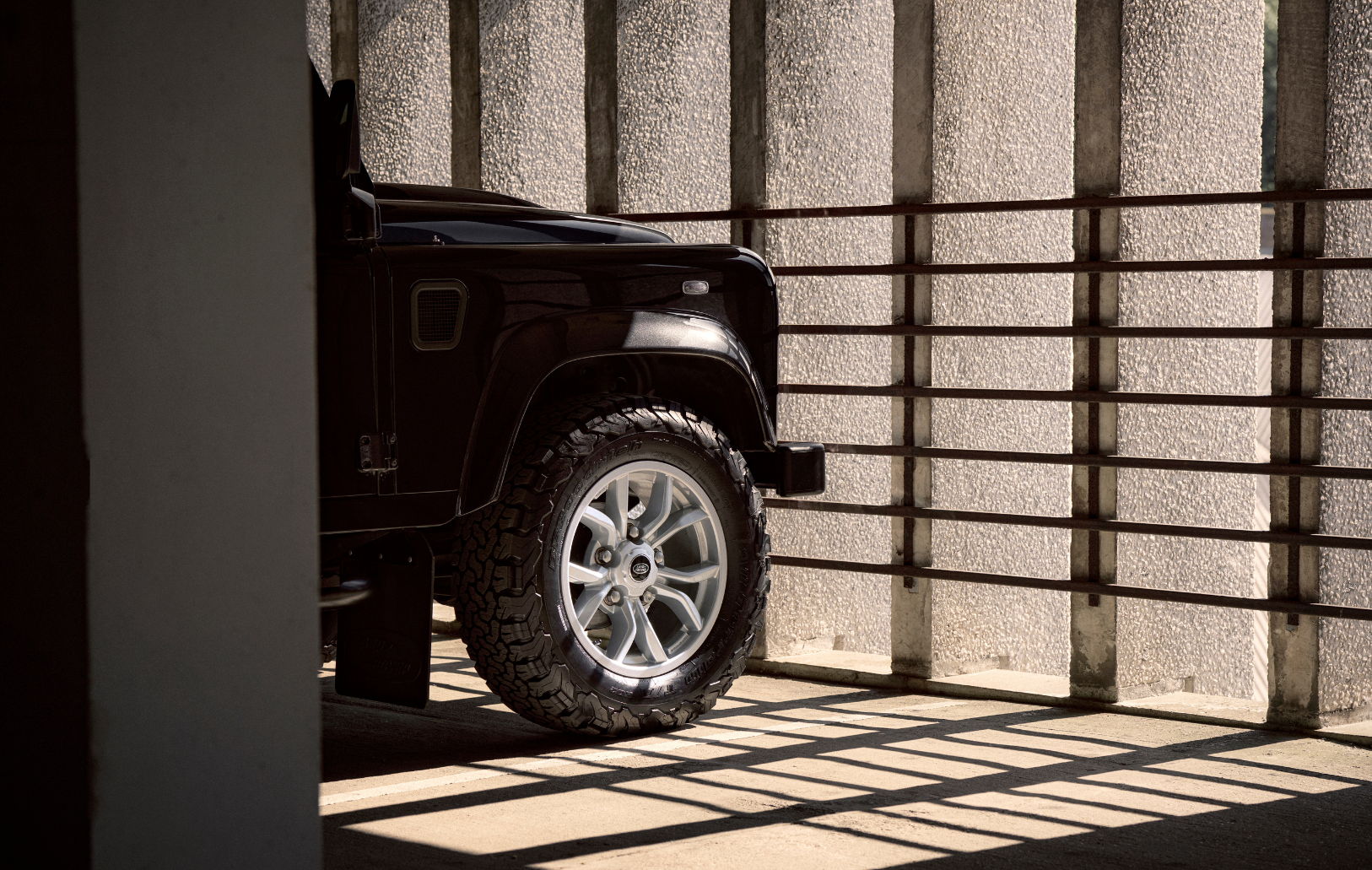 Front right tire of a black Defender in a shadowed concrete setting.