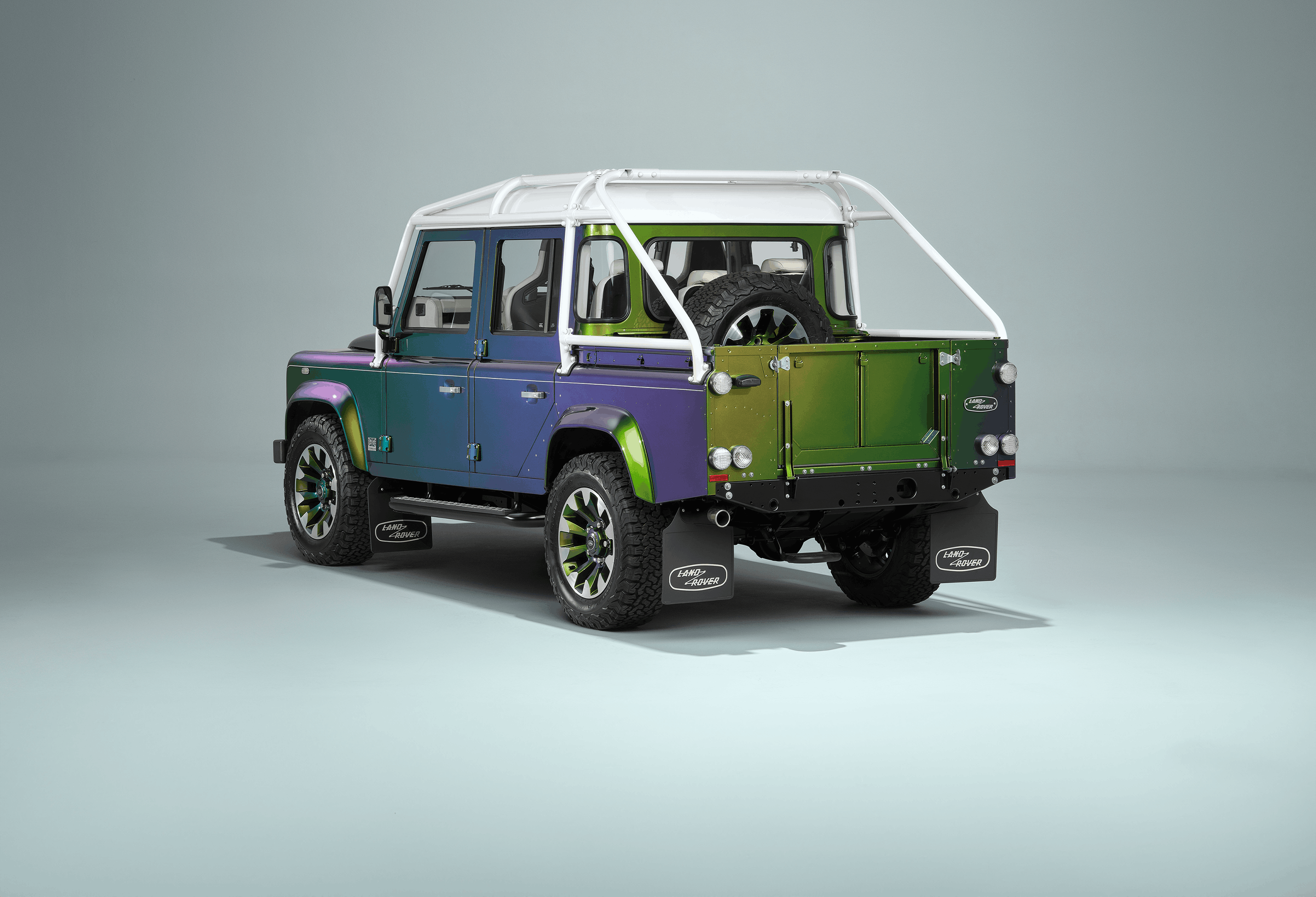 A green Defender V8 on the beach.