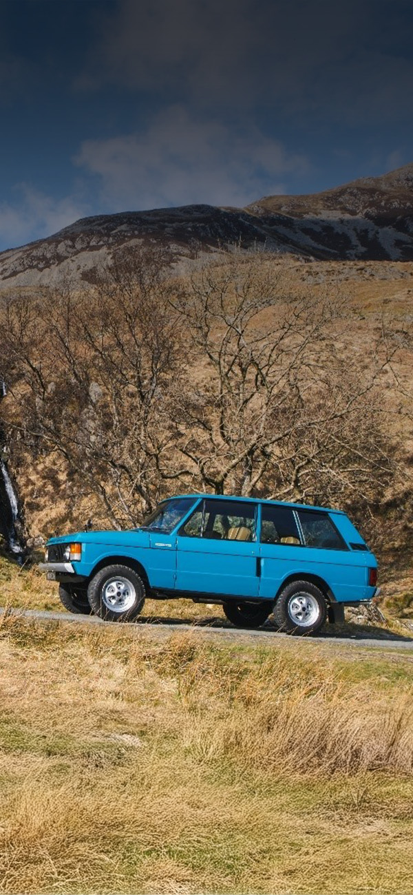 Blue Range Rover driving through rocky mountain road with waterfall in background.