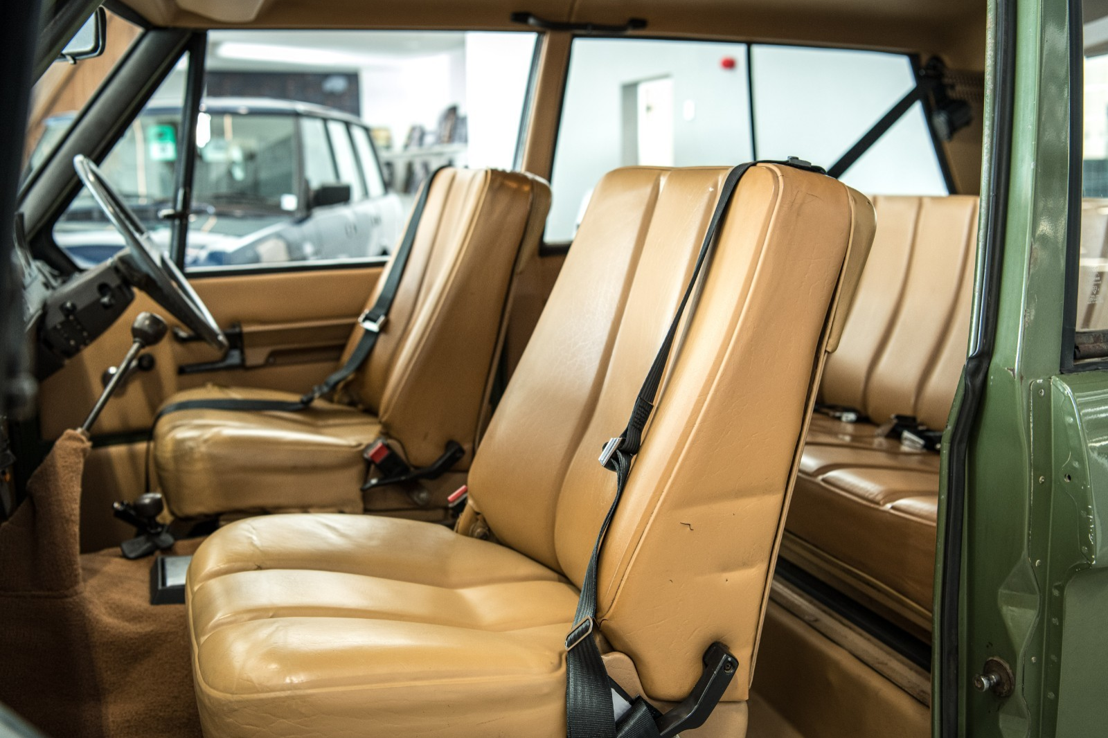 Tan leather Range Rover interior with two front seats and rear bench, door open showing green exterior.